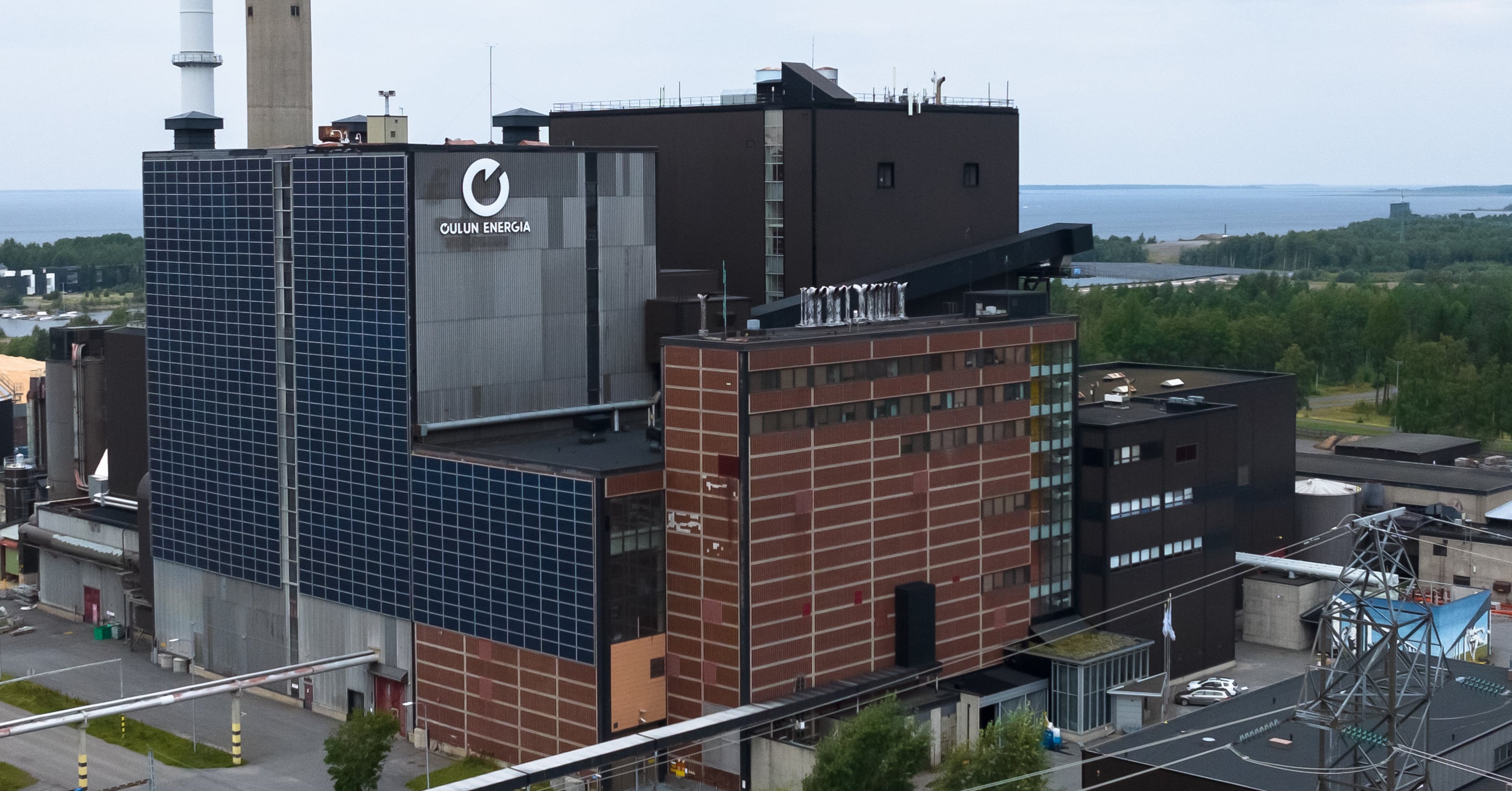 Kuvassa näkyy Oulun Energian Toppilan voimalaitoksen julkisivu ja takana meri. 