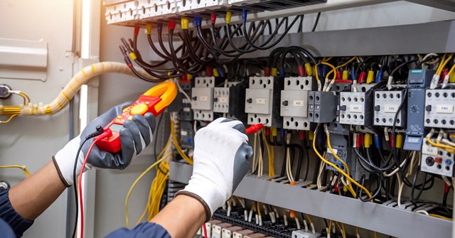 Sähköalan työntekijä mittaamassa mittalaitteella, työntekijästä näkyy kuvassa ainoastaan kädet.