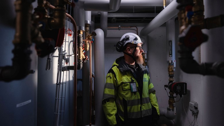 Työntekijä seisoo teknisessä tilassa putkien, venttiilien ja laitteiden keskellä suojavarusteet yllään.