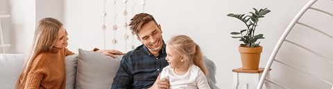 Vanhemmat ja lapsi istuvat sohvalla ja hymyilevät toisilleen. 