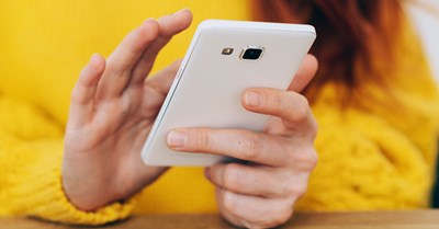 A person with a yellow shirt is scrolling through their white phone.