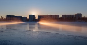 Kuvassa näkyy oululaisia kerrostaloja ja jäinen vedenpinta, johon auringonsäteet osuvat.  